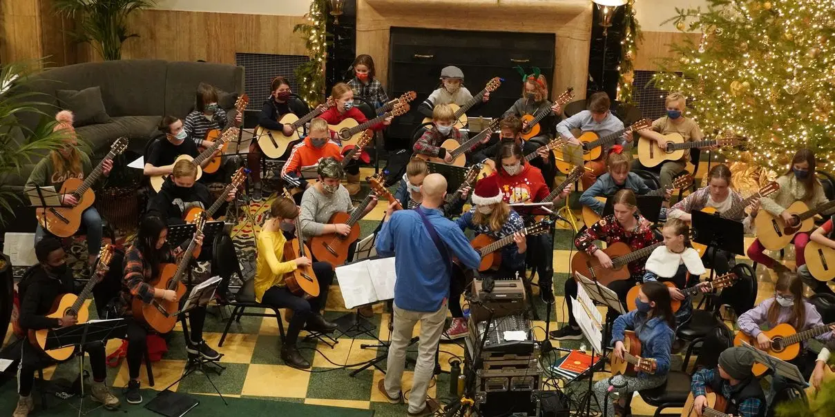 A group of people playing guitars with a conductor in front, festive setting.
