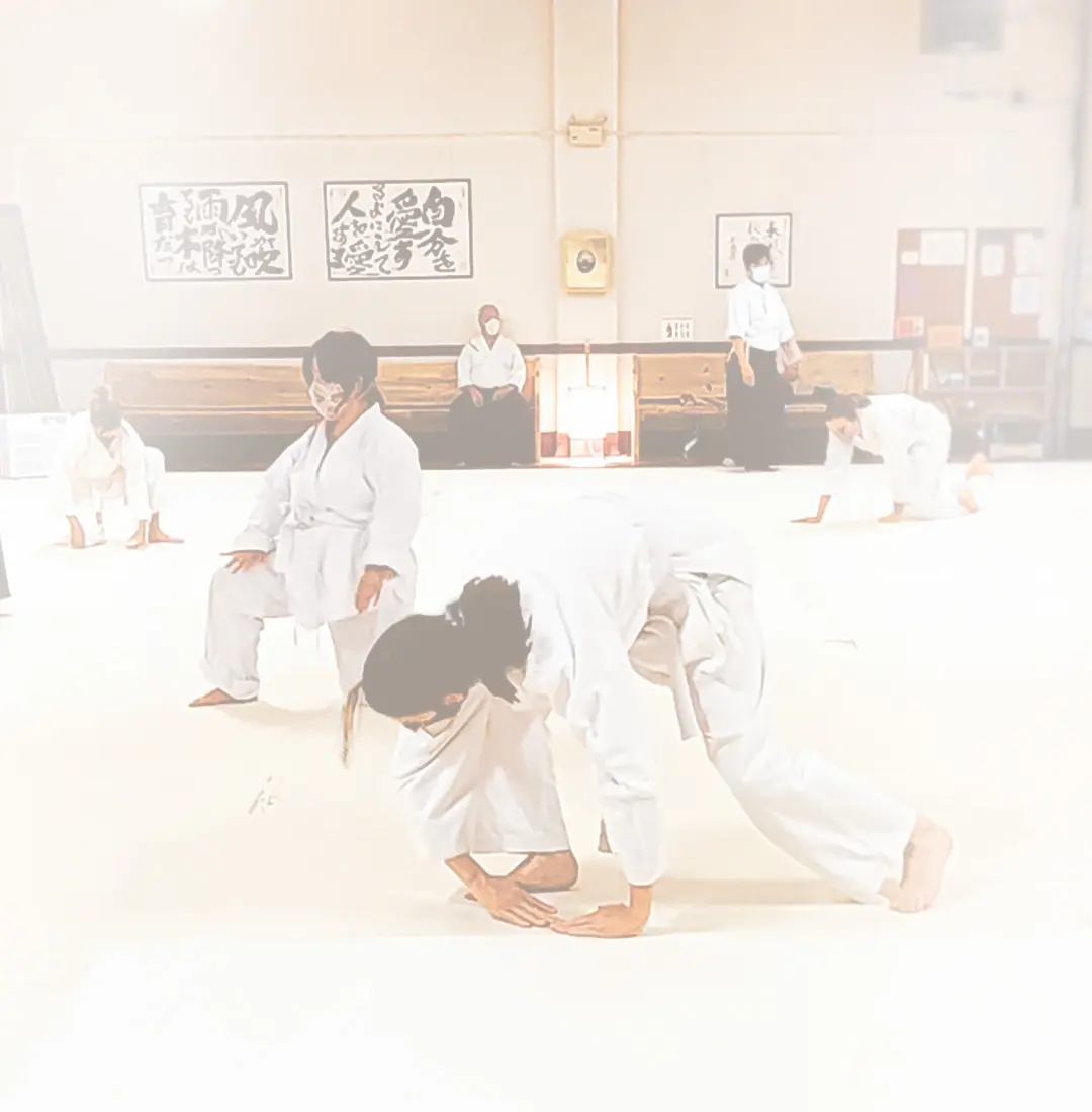 People in white uniforms are practicing martial arts in a studio.