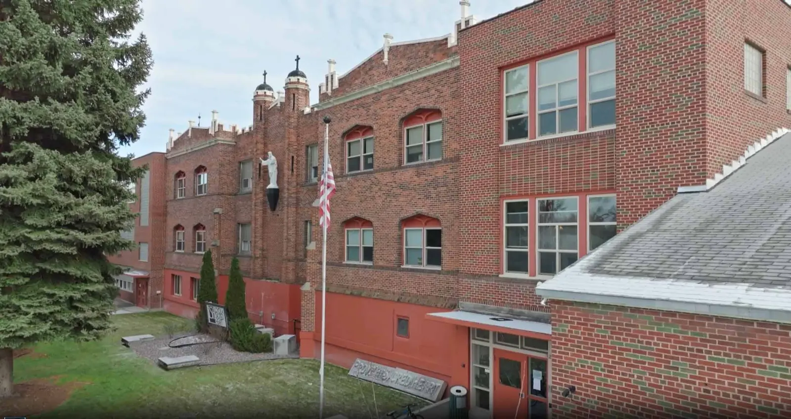 A red brick building features a statue and an American flag in the front lawn.