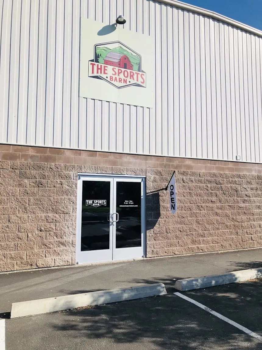 The exterior of a building with a sign that reads The Sports Barn above the entrance doors.