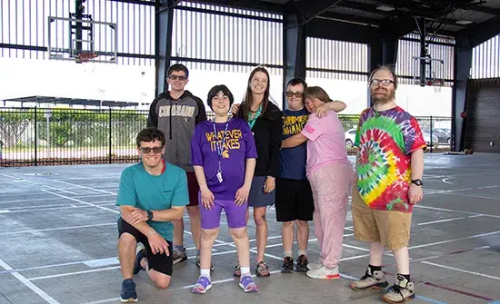 A group of adults stands together on an outdoor basketball court.