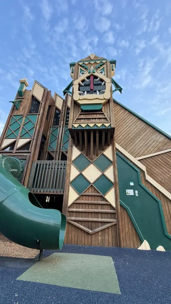 A wooden playground structure with a slide is shown against a blue sky.