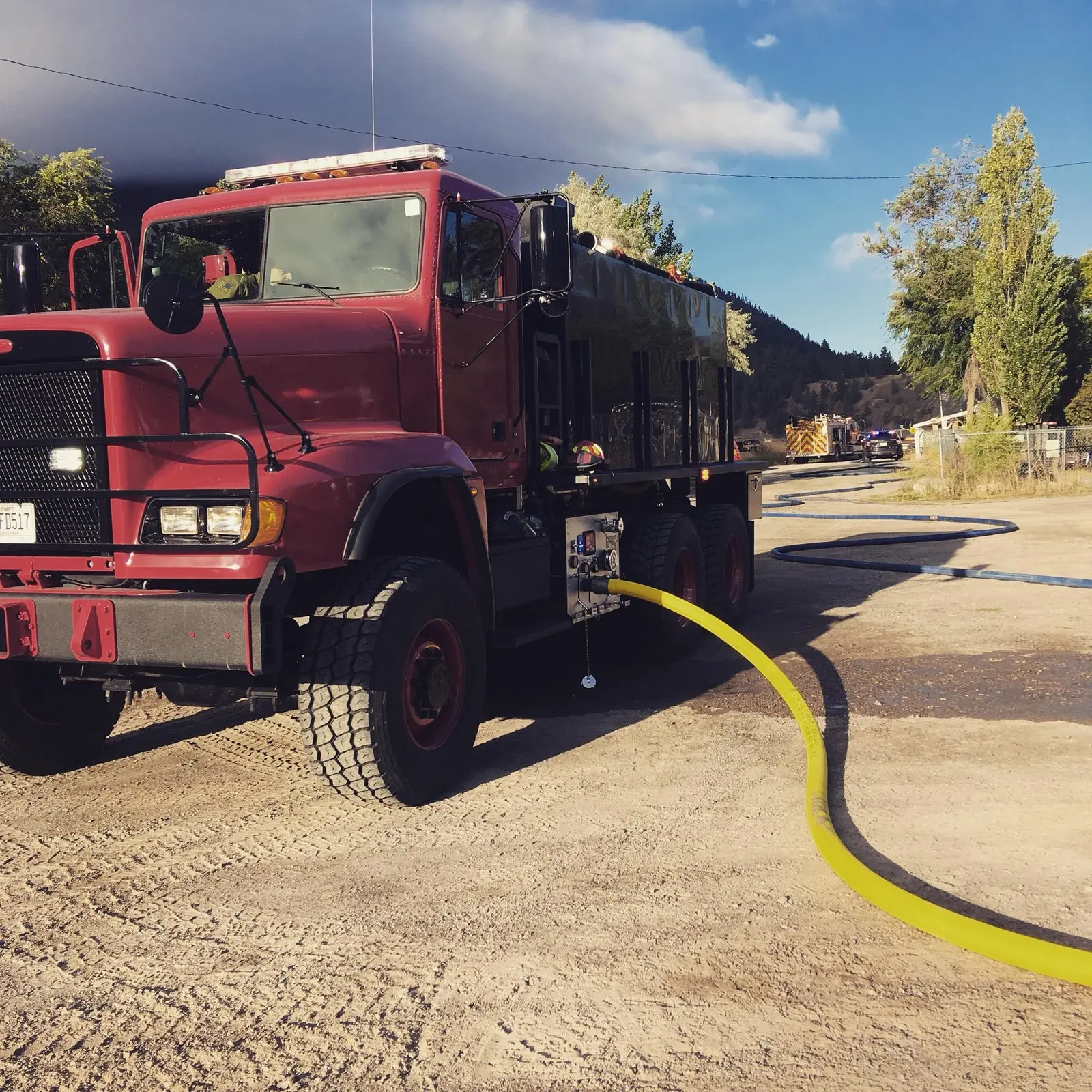 A red fire truck is parked on a dirt lot with a yellow hose connected to its side.