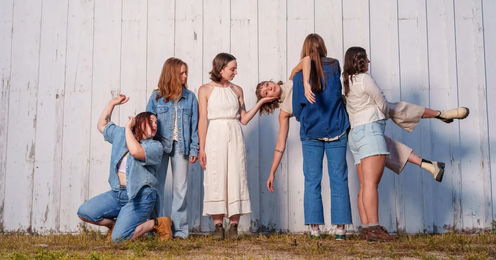 A group of young women are posing together in a line in front of a white barn wall.