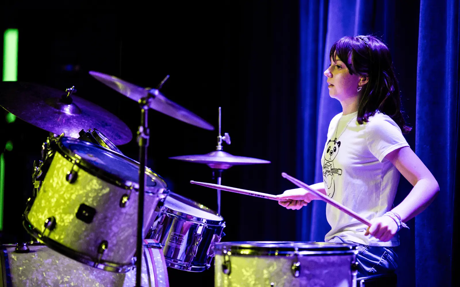 A person plays drums on stage under colored lights.