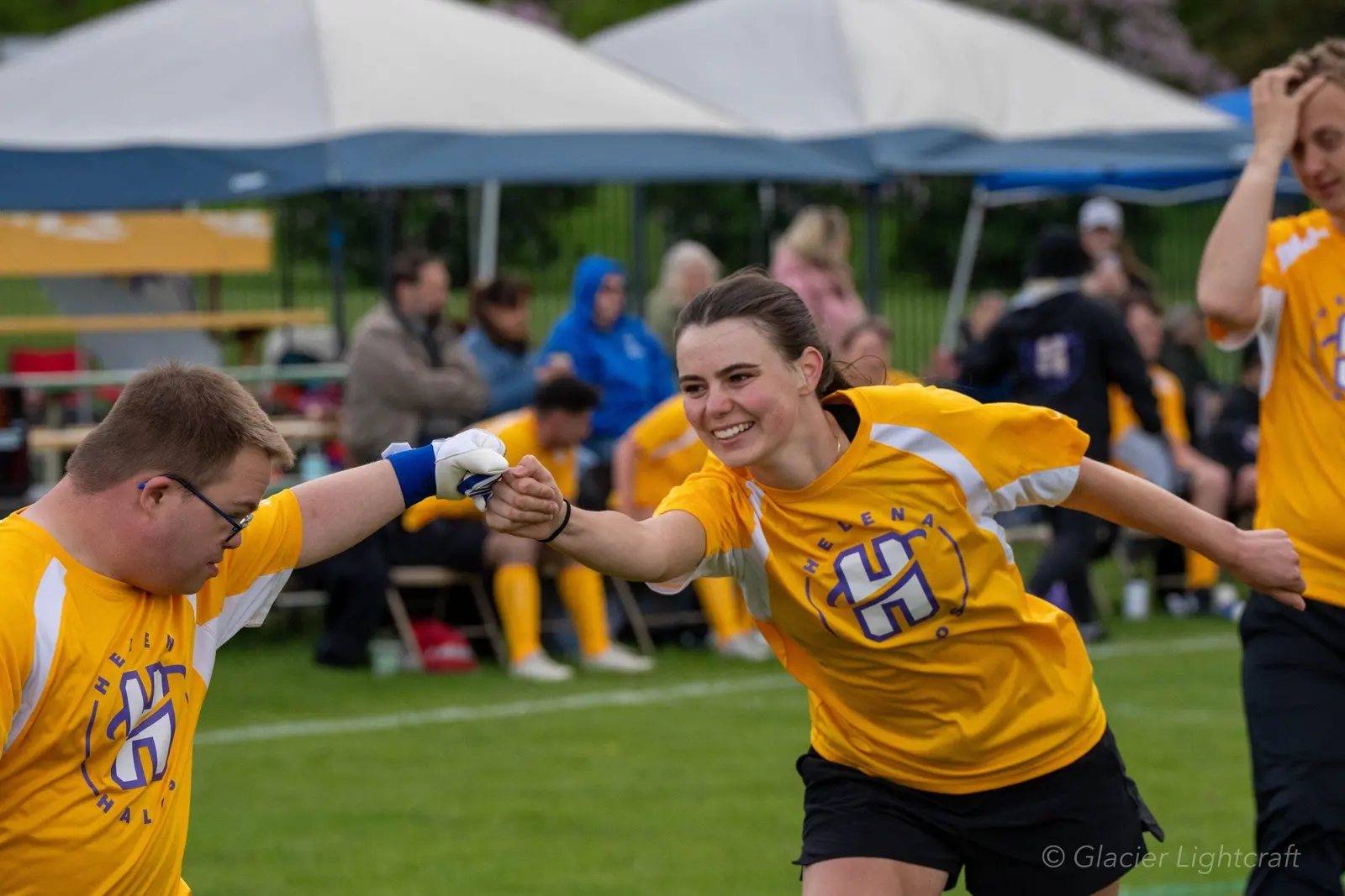 Two athletes in matching yellow jerseys fist bump on a sports field.