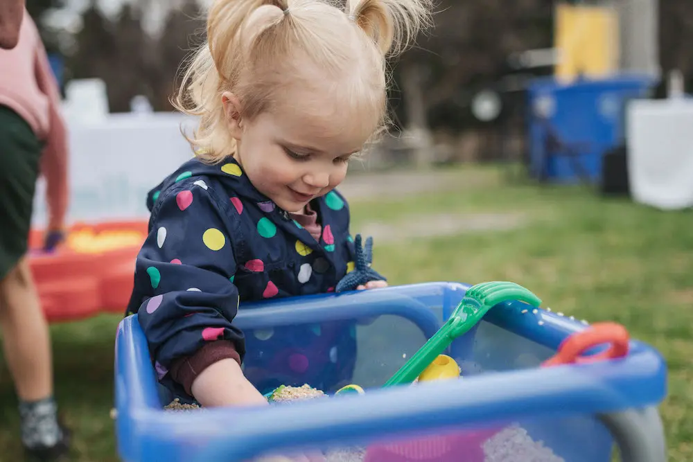 A young child plays with toys in a blue container outdoors.