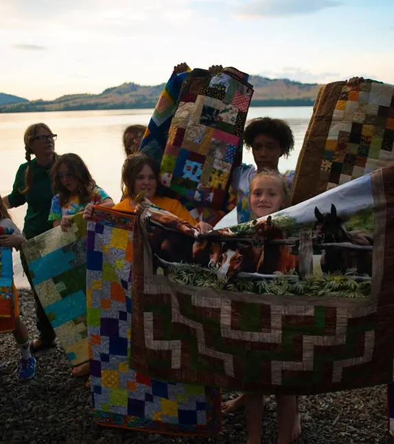 Grace Campers smile while holding up their quilts at campfire.
