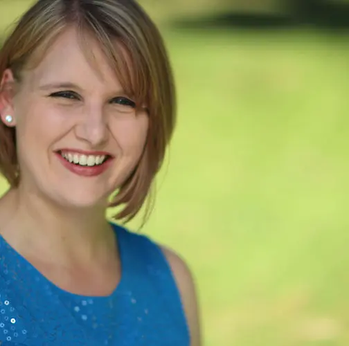 A smiling woman is shown in a portrait shot against a blurry green outdoor background.