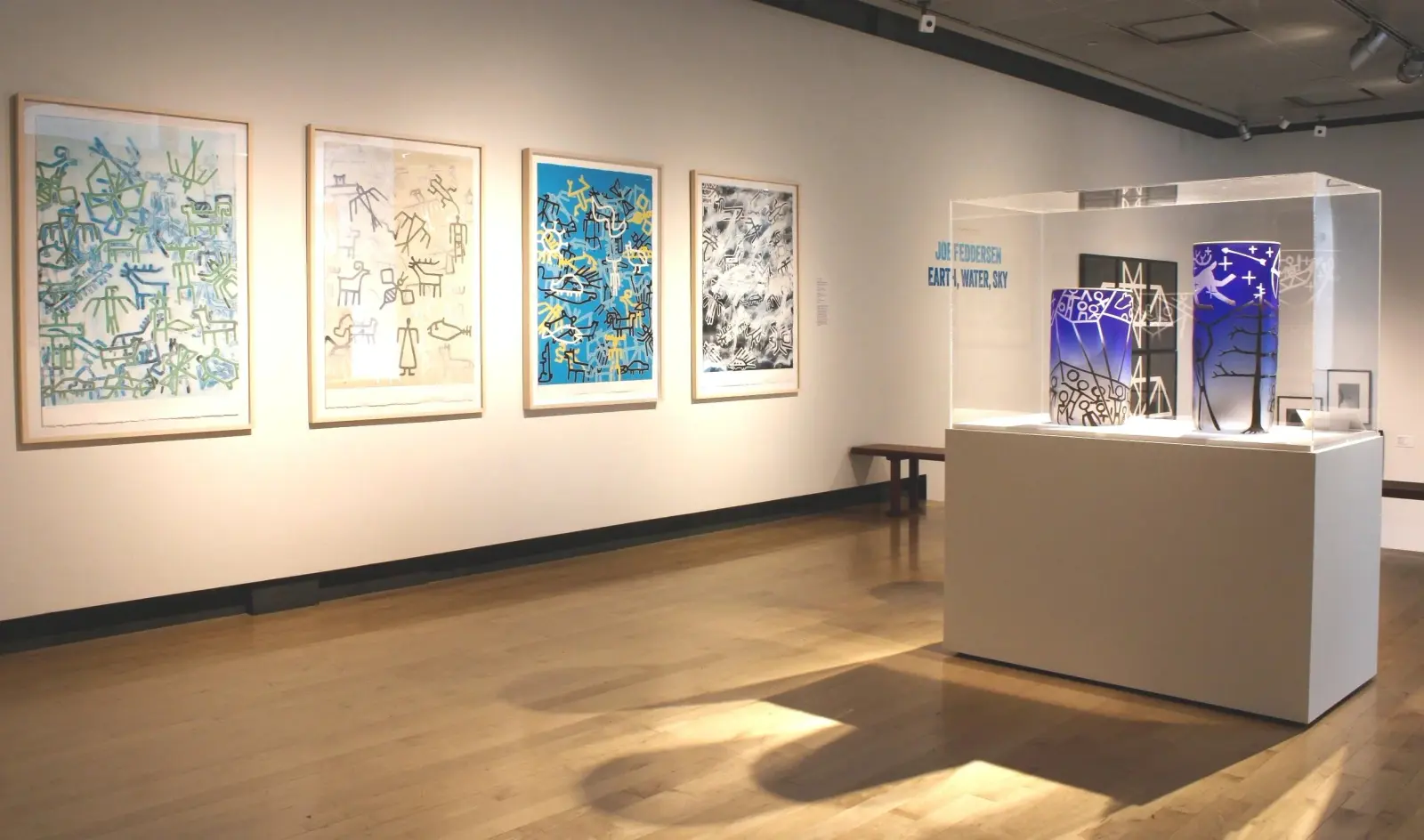 A gallery exhibit features framed prints on a wall and glass sculptures on a display pedestal.