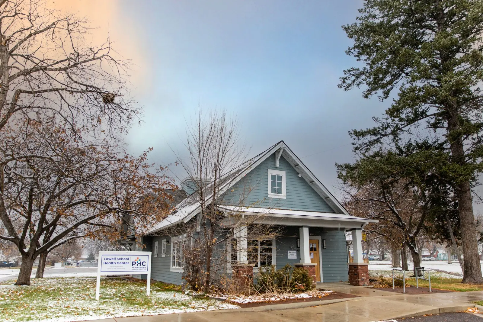 A blue building with a sign identifying it as a health center sits on a snowy lawn.