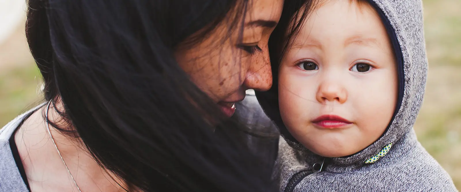 A woman and a young child in a hooded jacket look closely at one another.