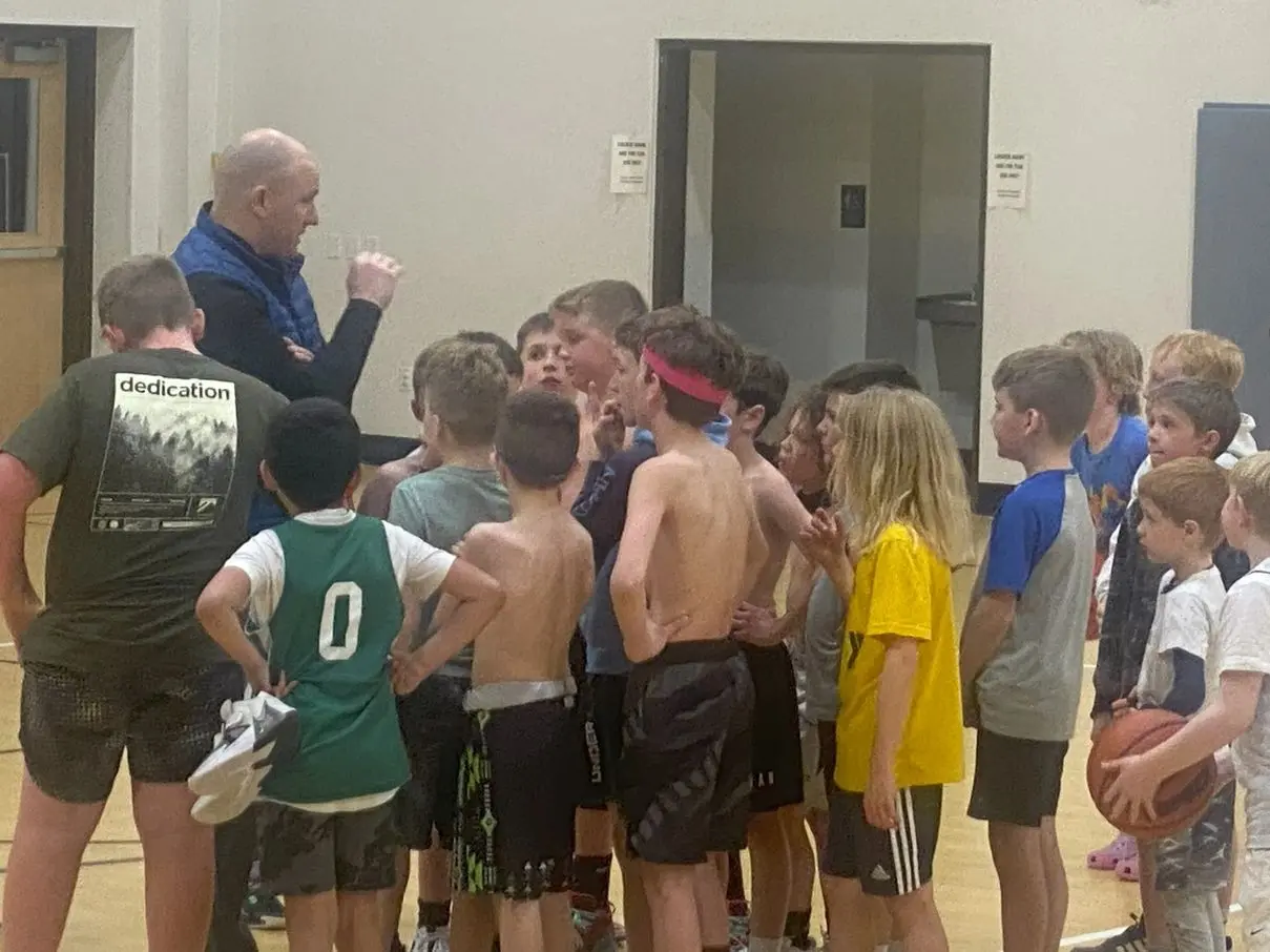 Coach giving instructions to young basketball players in gym.