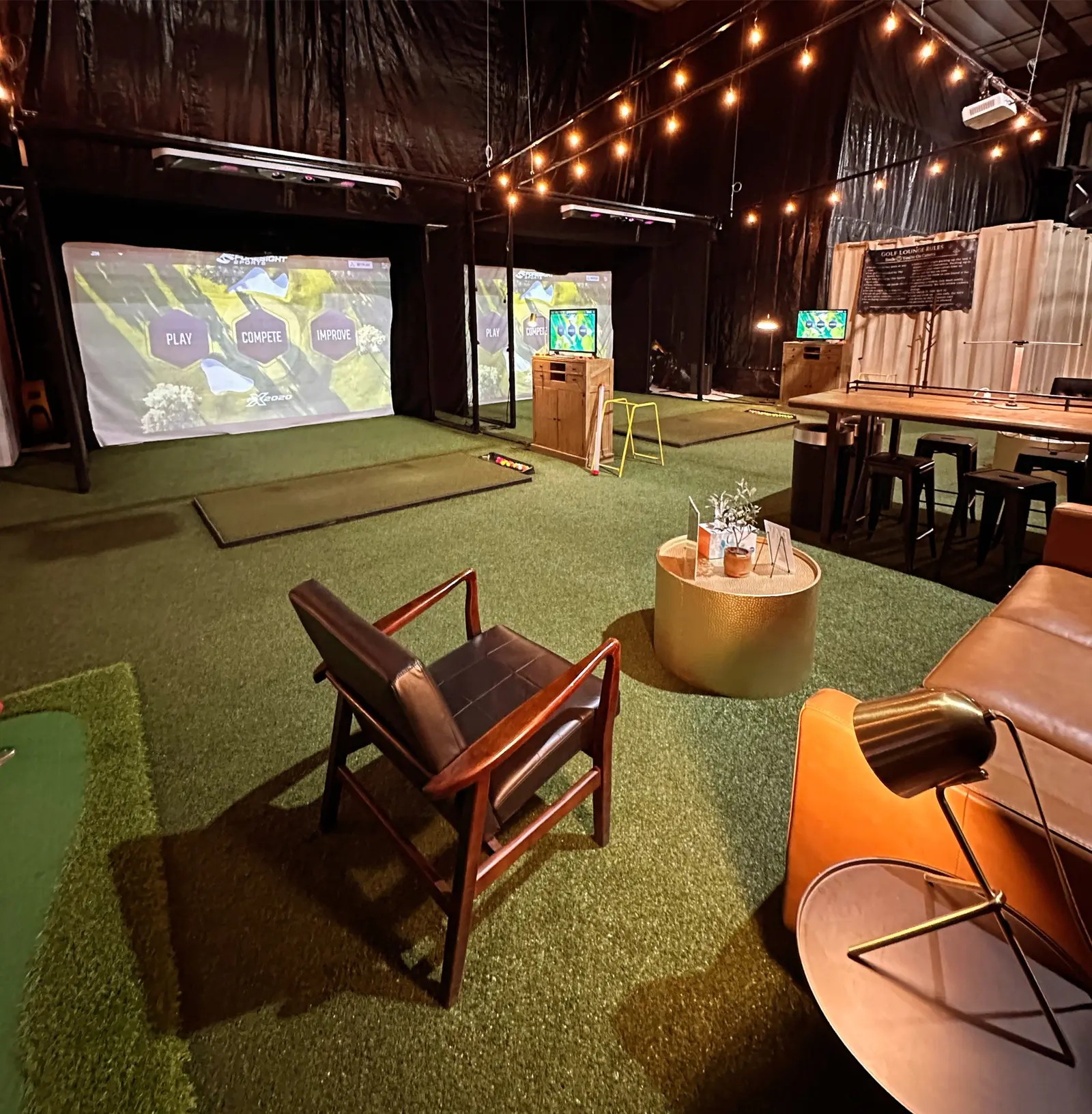 A bright indoor golf lounge with projection screens and comfortable seating.