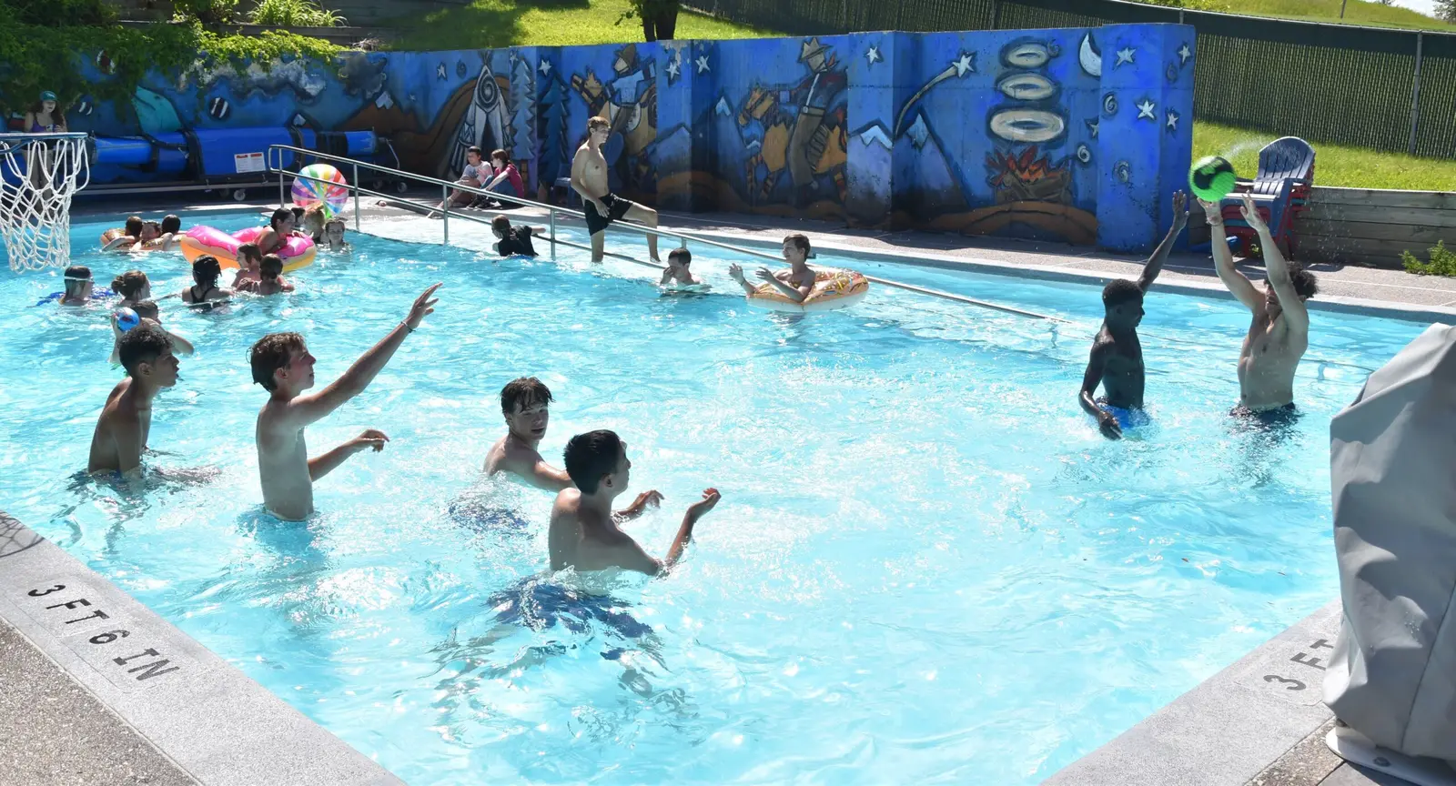 A group of teenagers enjoys playing with a ball in an outdoor swimming pool.