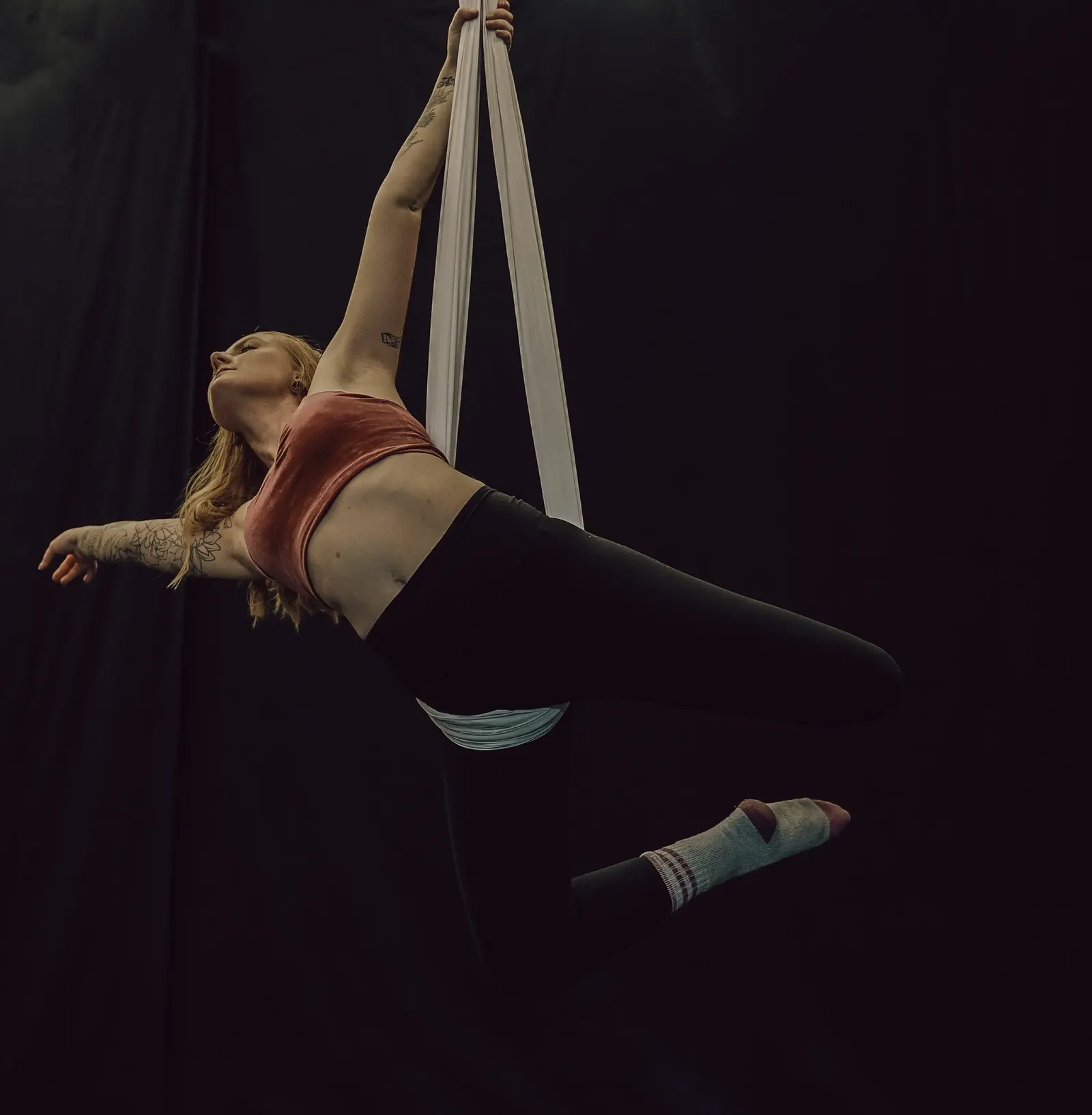 A woman practices aerial silks against a dark background.
