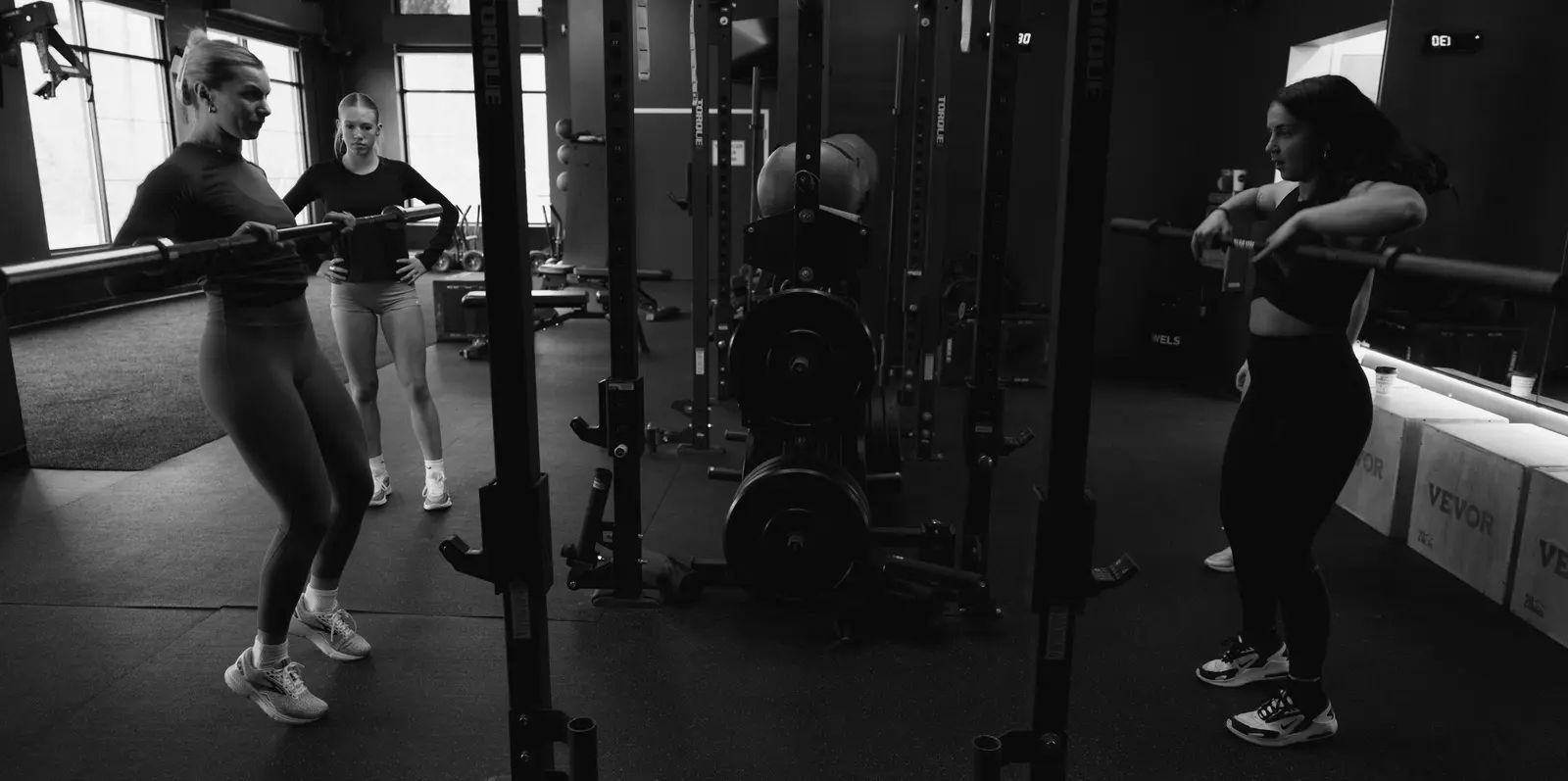 Three people are training with barbells in a gym.