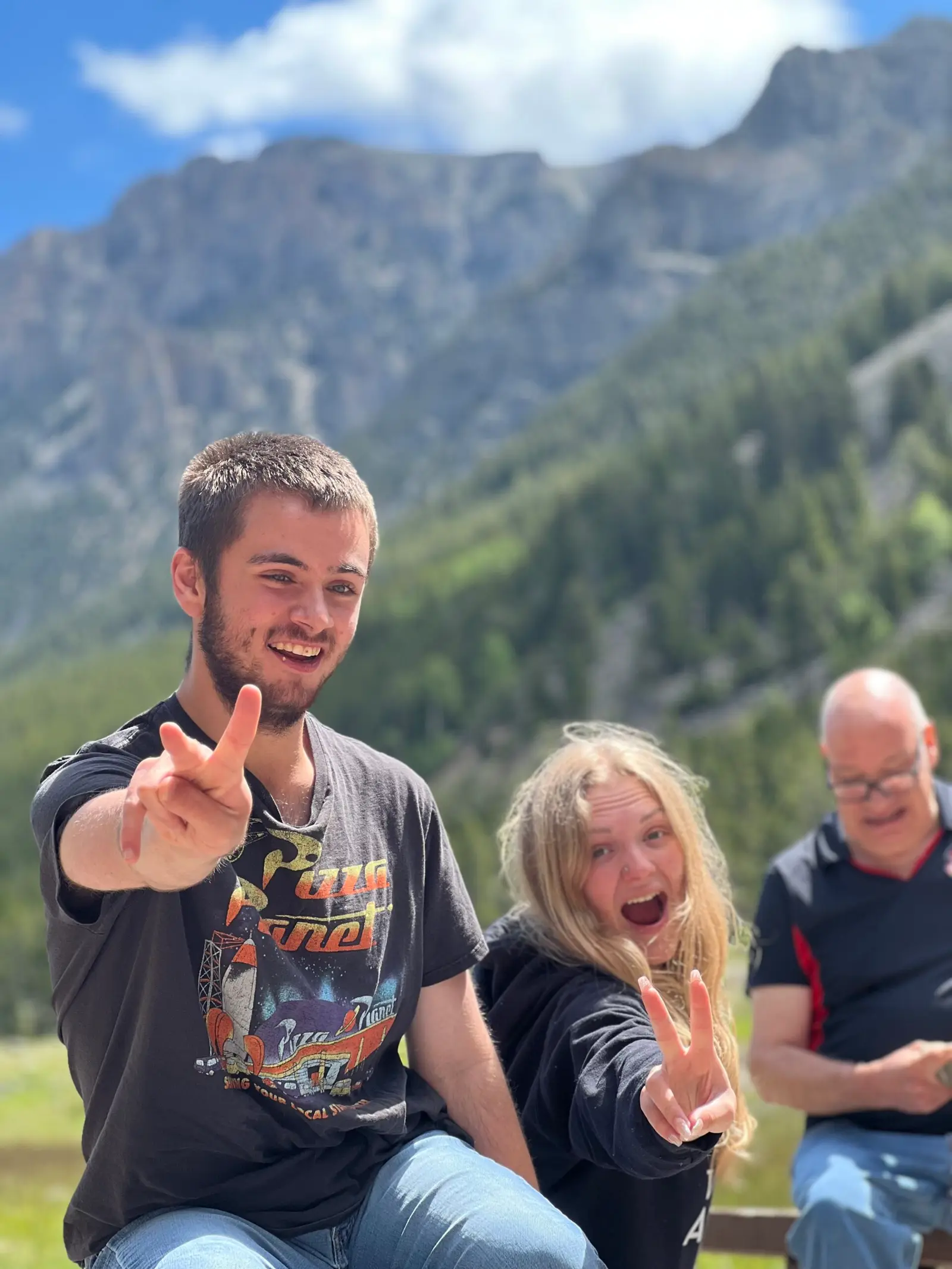 Two young people and an older man pose for a photo in front of a mountain.