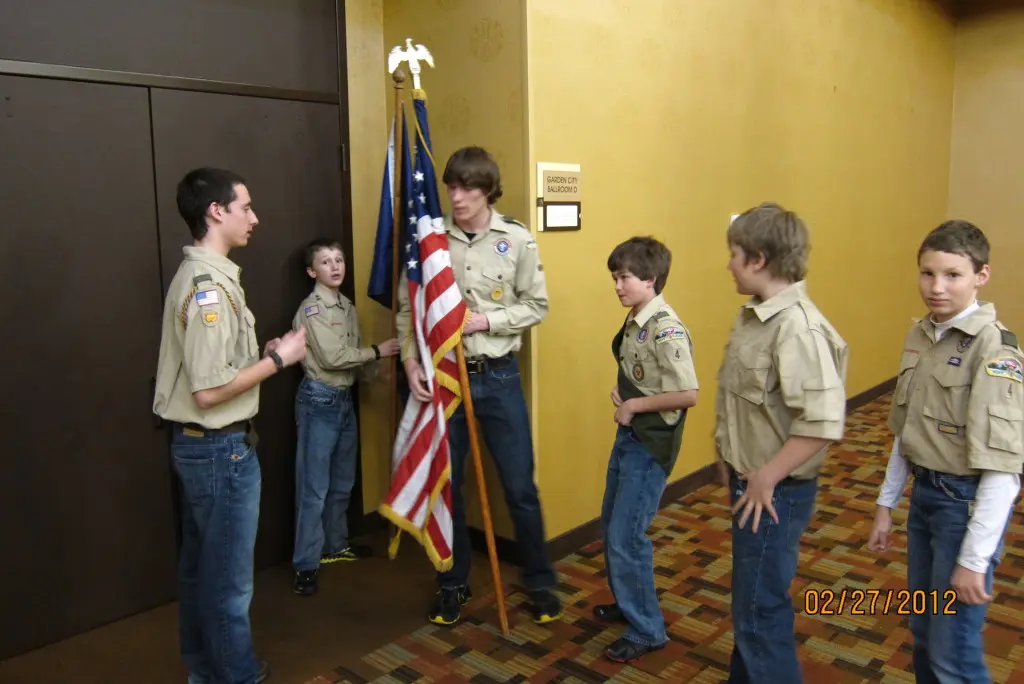 A group of boys in scouting uniforms are standing together holding an American flag.