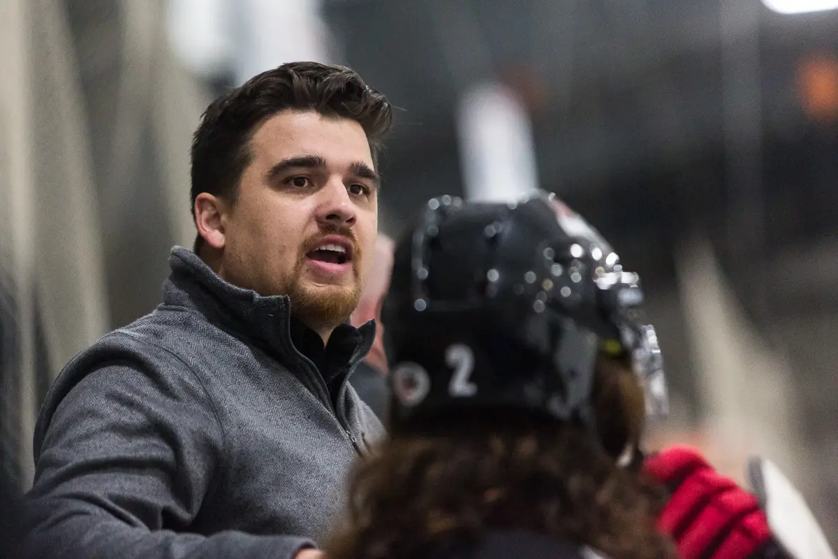 A coach speaks to a hockey player wearing a helmet.