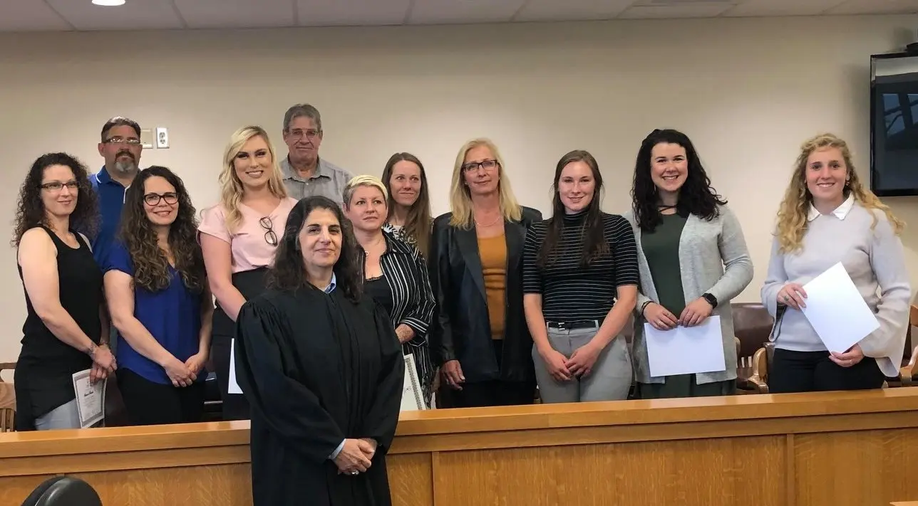 A group of adults standing behind a wooden railing in what appears to be a courtroom.