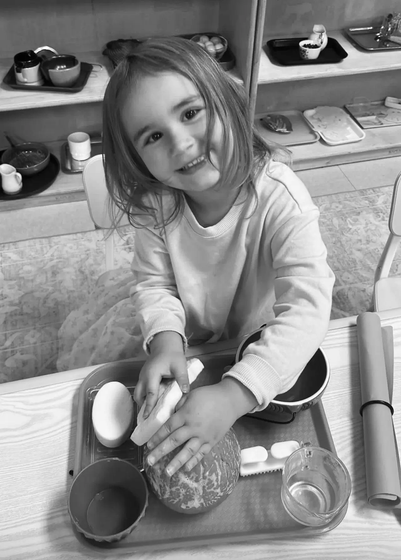 A smiling child performs a cleaning activity in a classroom setting.