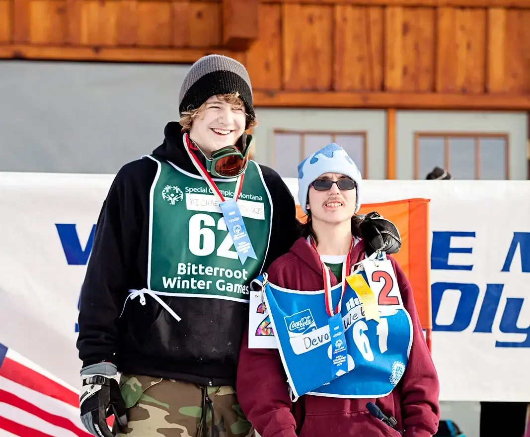 Two athletes wearing competition bibs and medals pose together at a winter sports event.