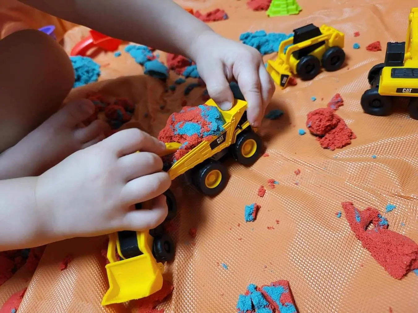 A child is playing with toy construction vehicles and colorful kinetic sand.
