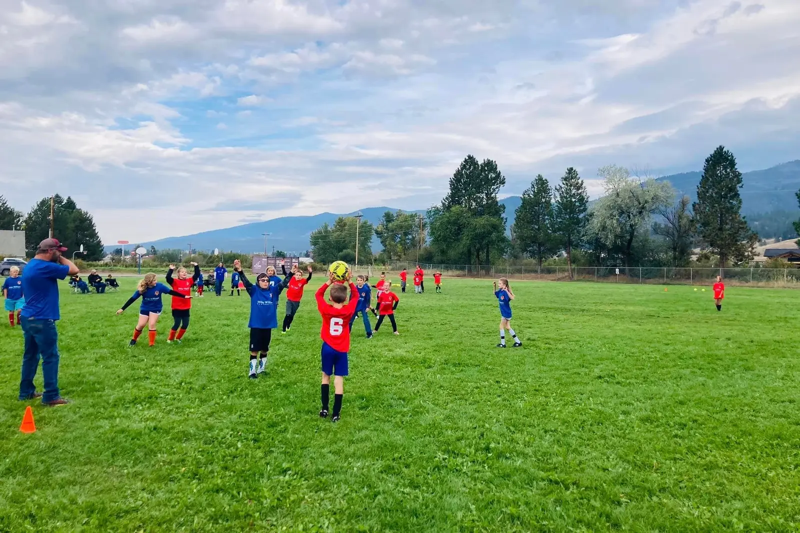 A group of children actively playing soccer on a grassy field with an adult coach nearby.
