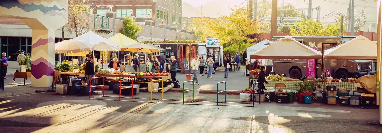 People browse stalls and food trucks at an outdoor farmers market.