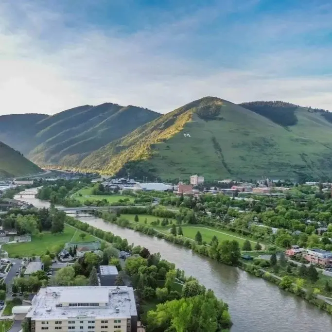 An aerial view of a town nestled in a valley with a river and mountains in the background.