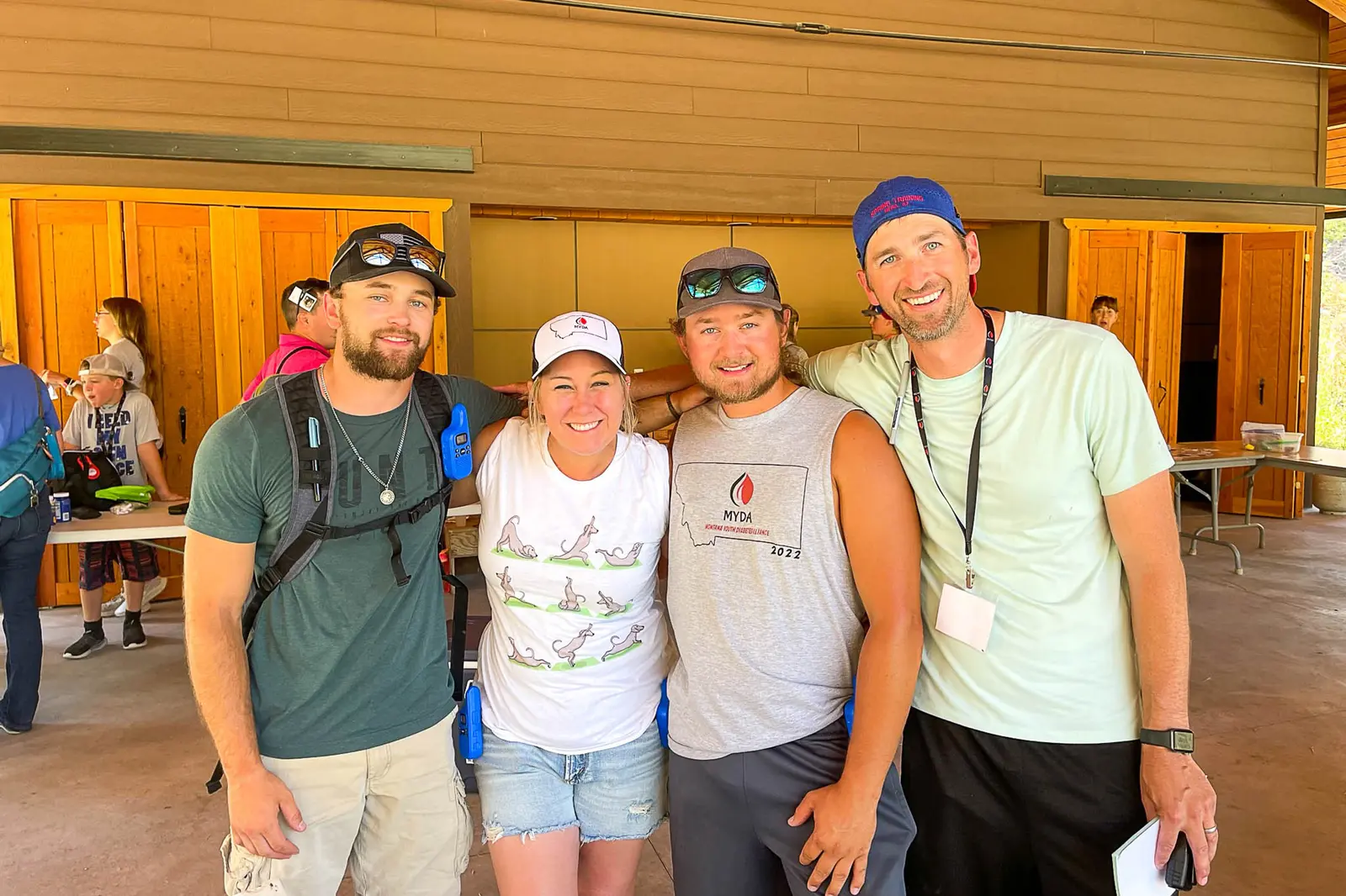 Four adults pose for a group photo outdoors in front of a wooden building.