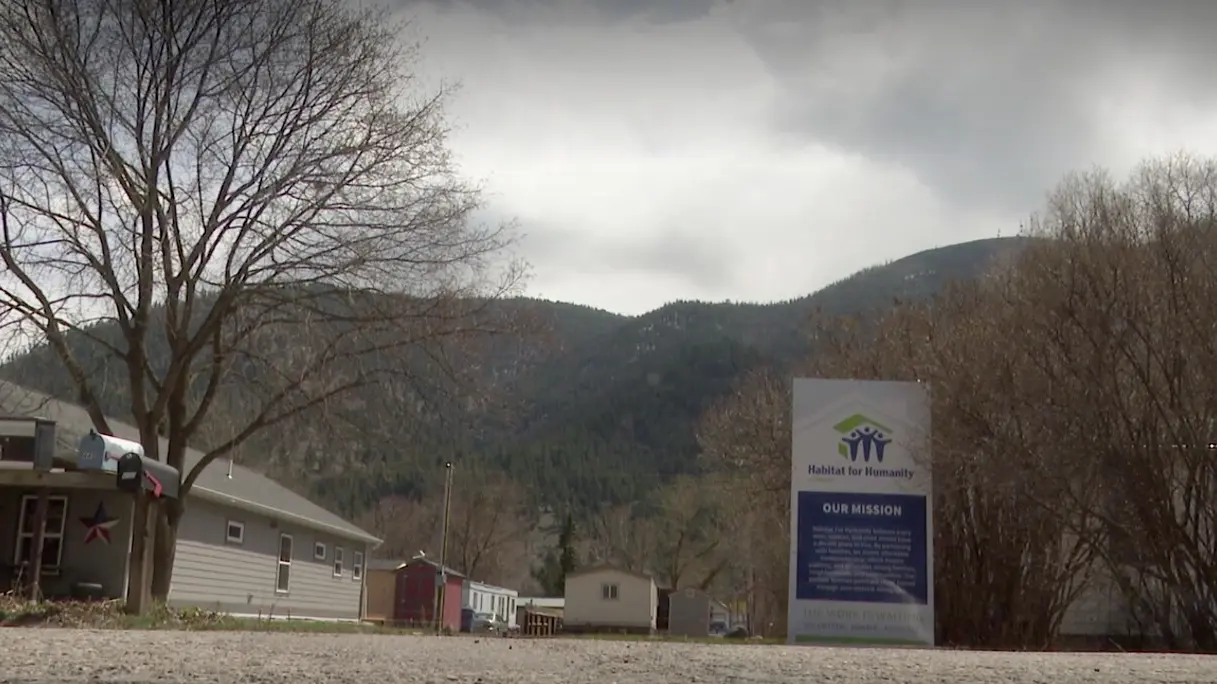 A Habitat for Humanity mission sign stands in a landscape with mountains in the background.