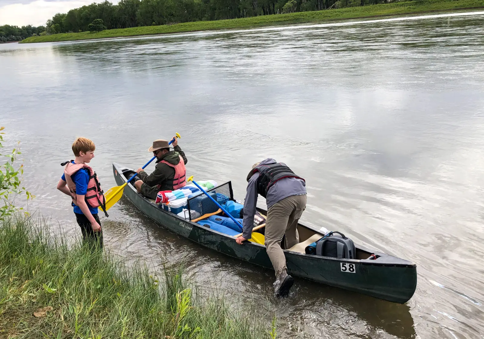 A child and two adults prepare to depart in a canoe on a river.