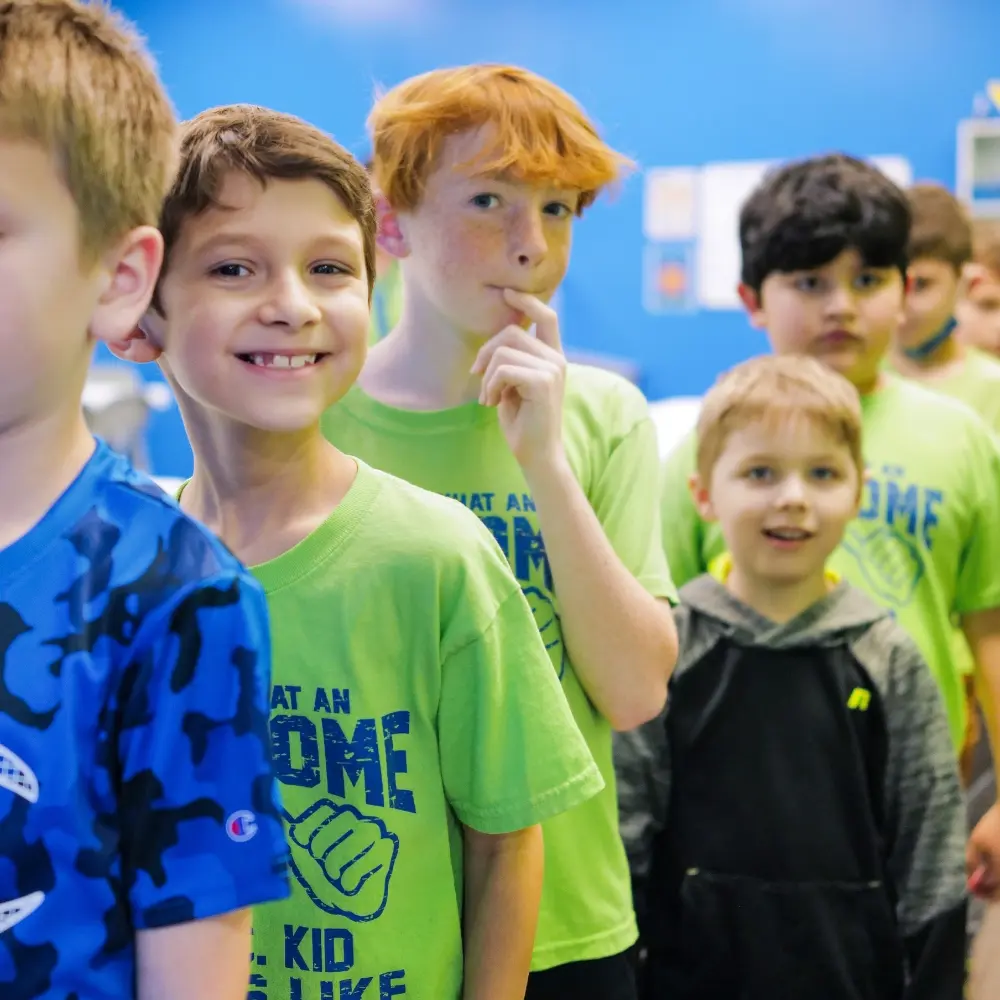 A group of children in matching shirts stand in a line indoors.