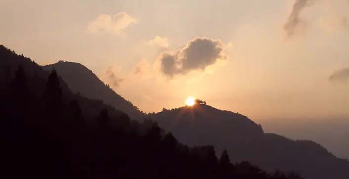 The sun sets behind a mountain range covered in trees.