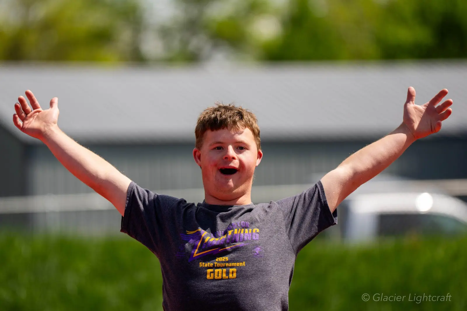 A young man celebrates with his arms outstretched while wearing a tournament t-shirt.