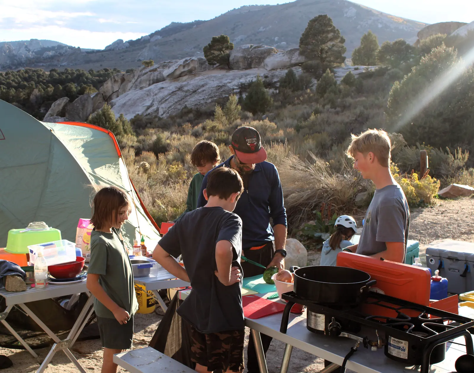A group of children and an adult are preparing food at a camping site.
