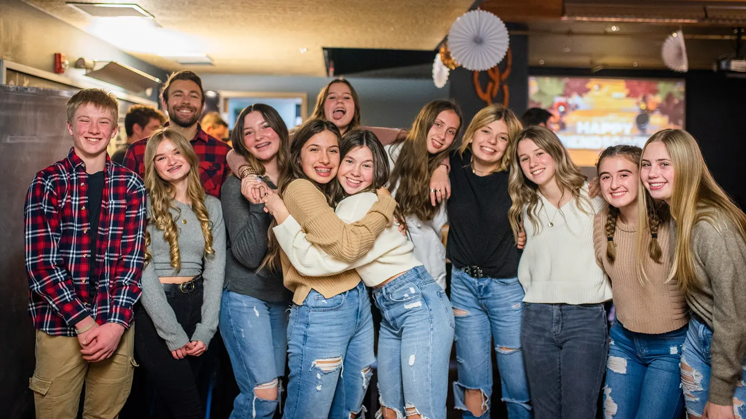 A group of teenagers and one adult pose together for a photo in an indoor setting.