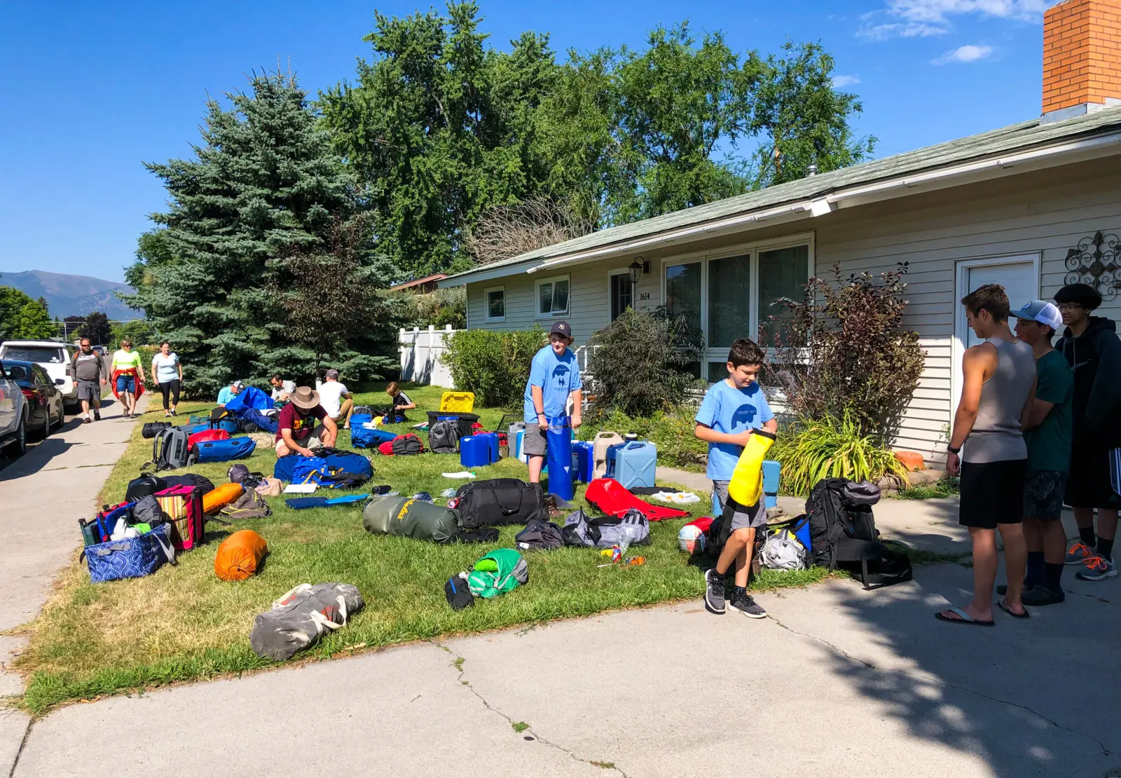 A group of boys organize camping equipment on a suburban lawn.