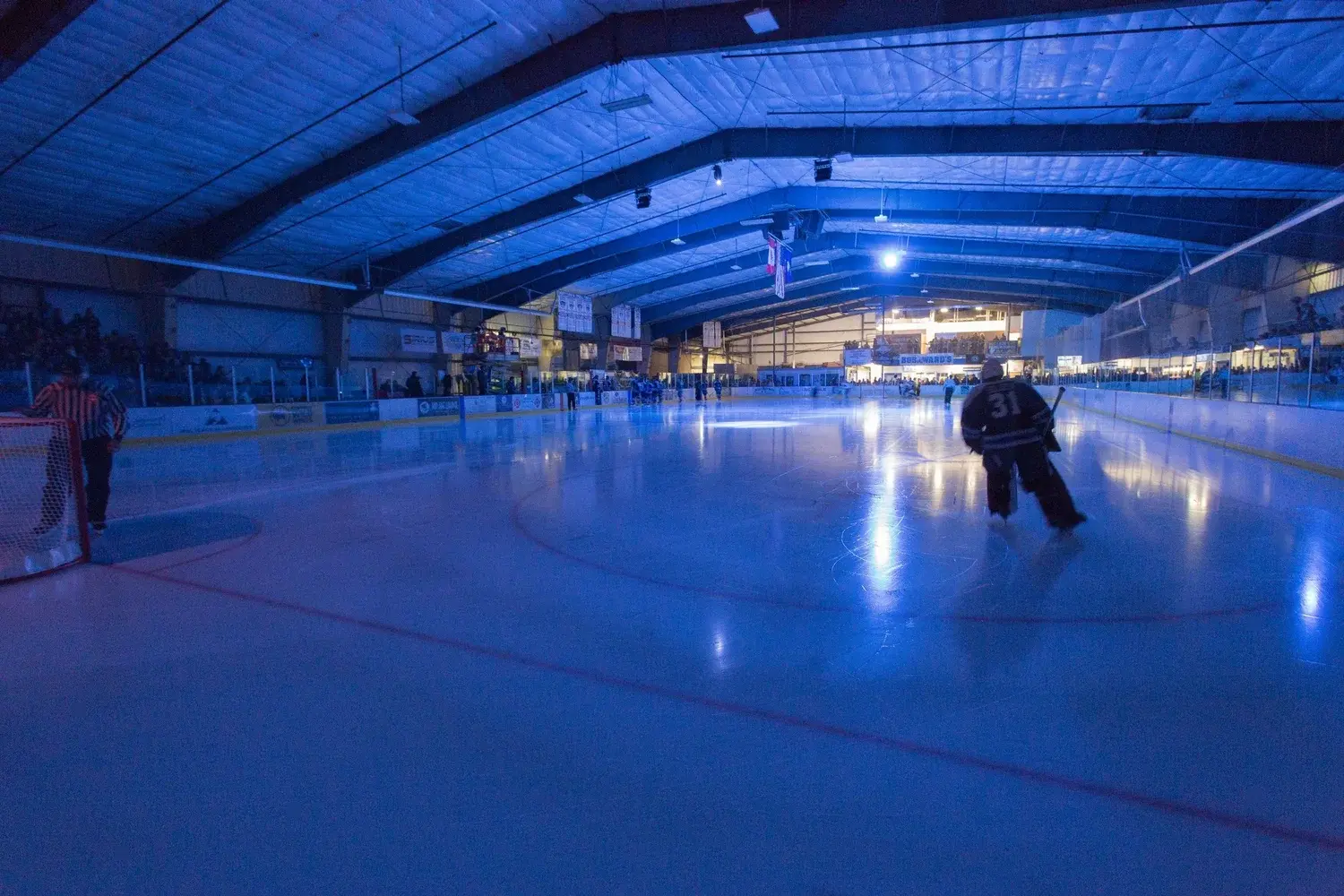 A hockey game is being played on an ice rink under blue lighting.