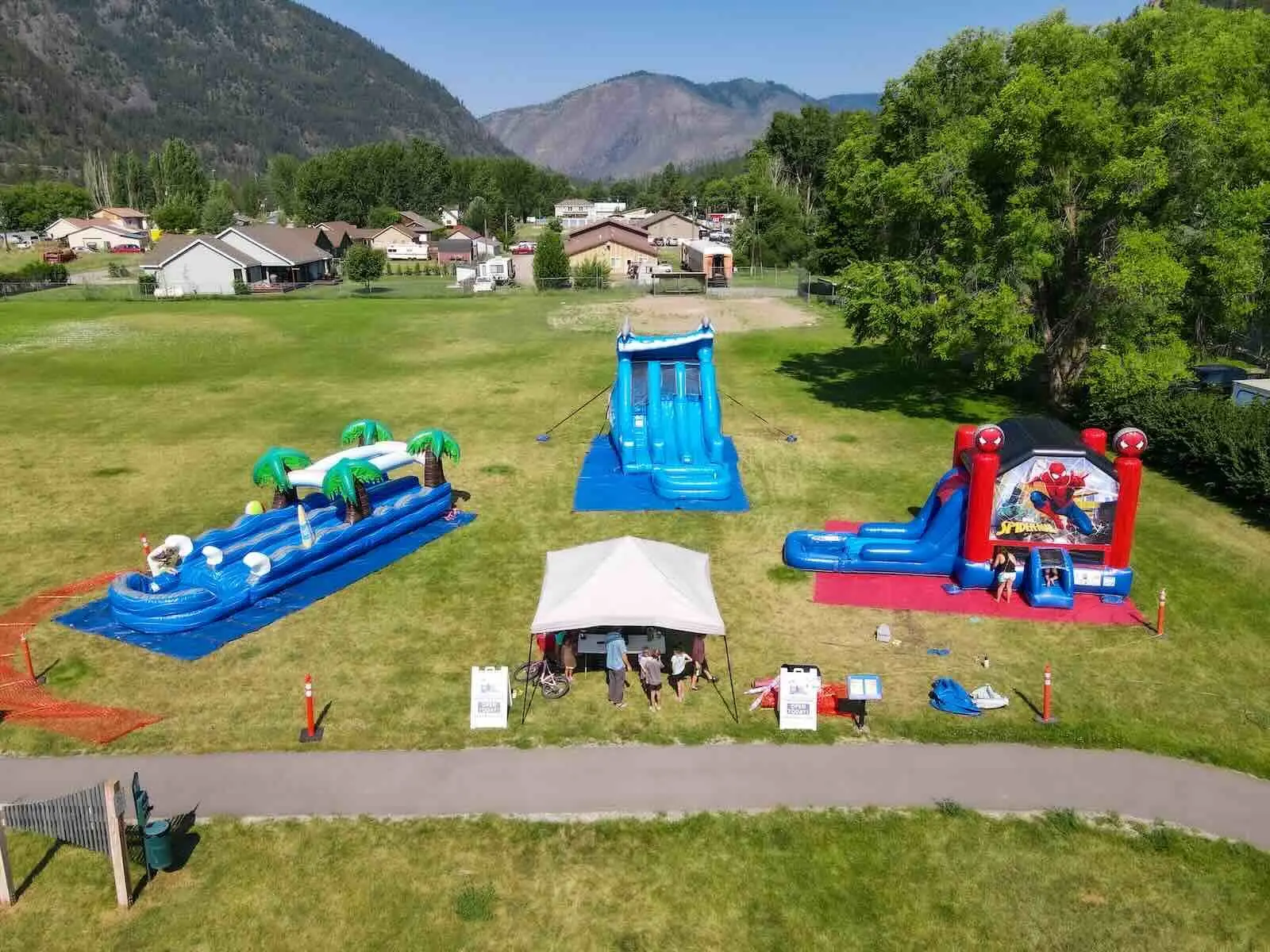 People gather under a tent in a park with several inflatable play structures set up on the grass.