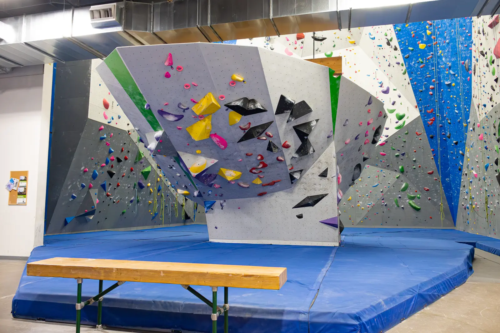 A view of an indoor rock climbing gym with colorful holds and a blue landing mat.
