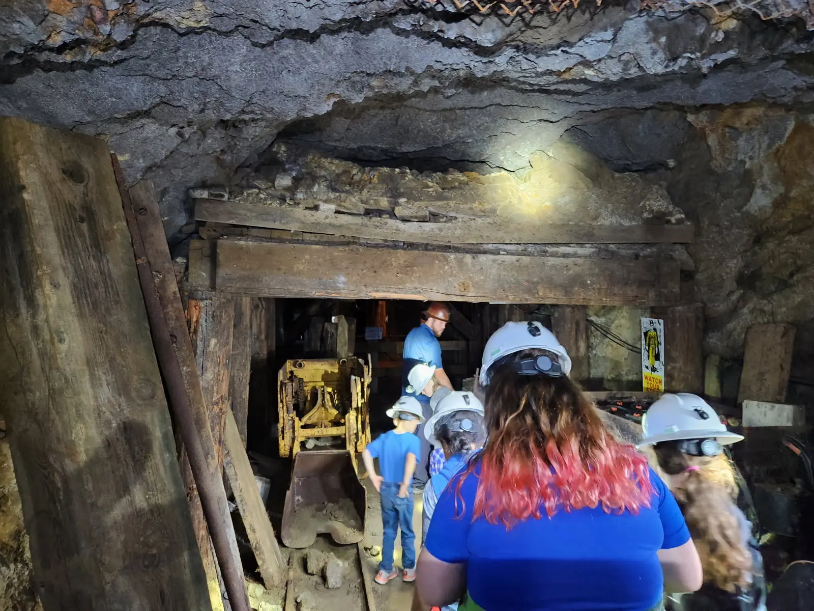 A group of people including children wearing hard hats explores the interior of a mine tunnel.