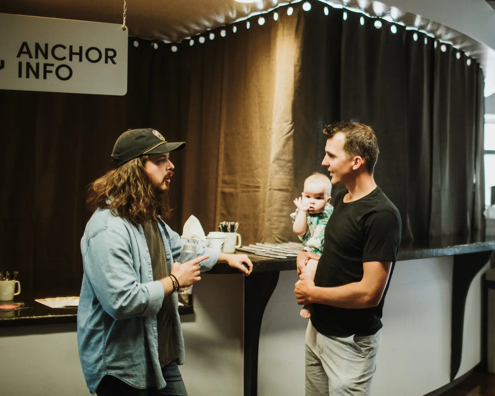 Two men have a conversation while one is holding a baby.