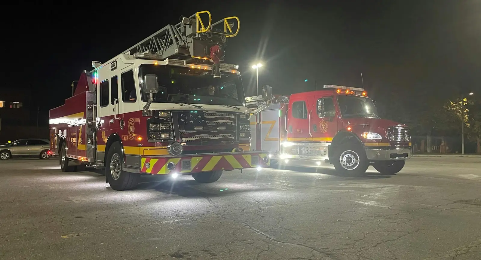 Two fire trucks are parked in a paved area at night.