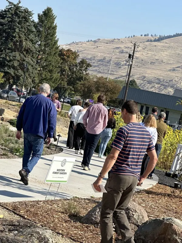 A group of people walks along a path past a garden sign.