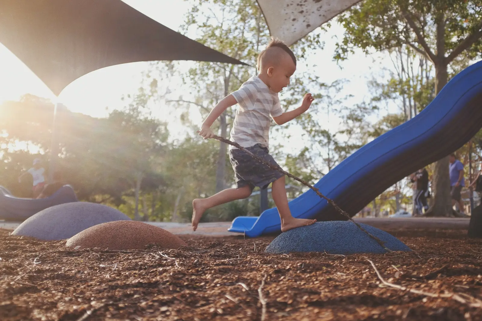 A young boy plays on a playground climbing structure while holding a long stick.