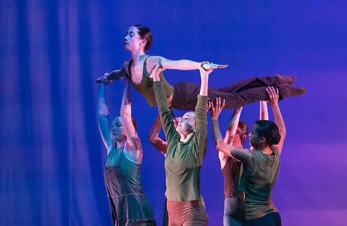 A group of dancers perform on stage with one dancer lifted horizontally above the others.