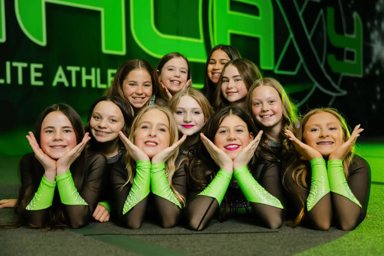 A group of young female athletes in green and black uniforms pose together for a photo.
